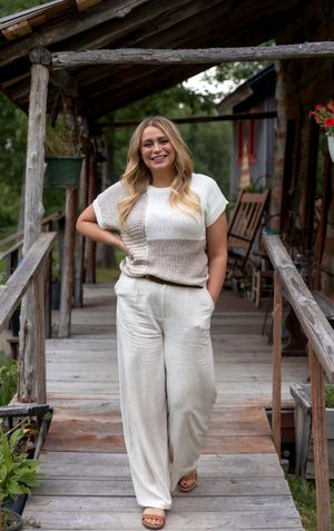 Fashion model poses on rustic wooden porch wearing casual white summer outfit and sandals.