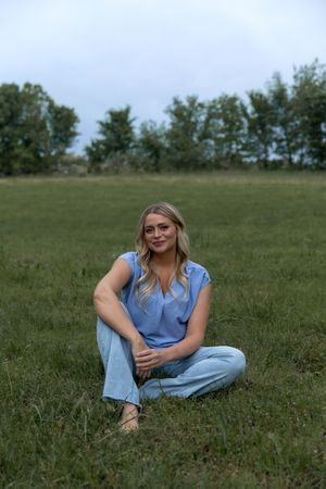 A person in a light blue top lounges casually on a grassy hillside on a summer day.