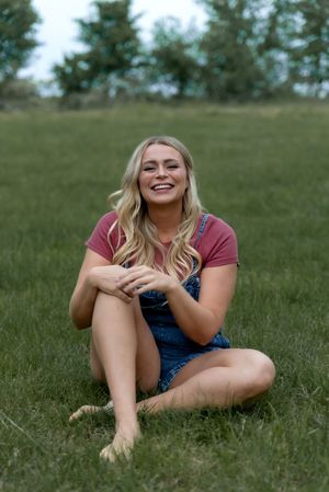 Candid outdoor photoshoot in grassy field wearing denim overalls and burgundy top.