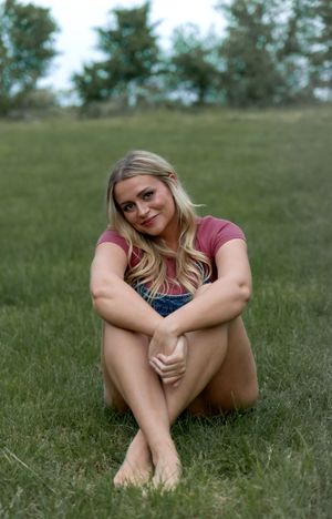 A person in casual attire sits relaxed in the grass during a warm afternoon photoshoot.