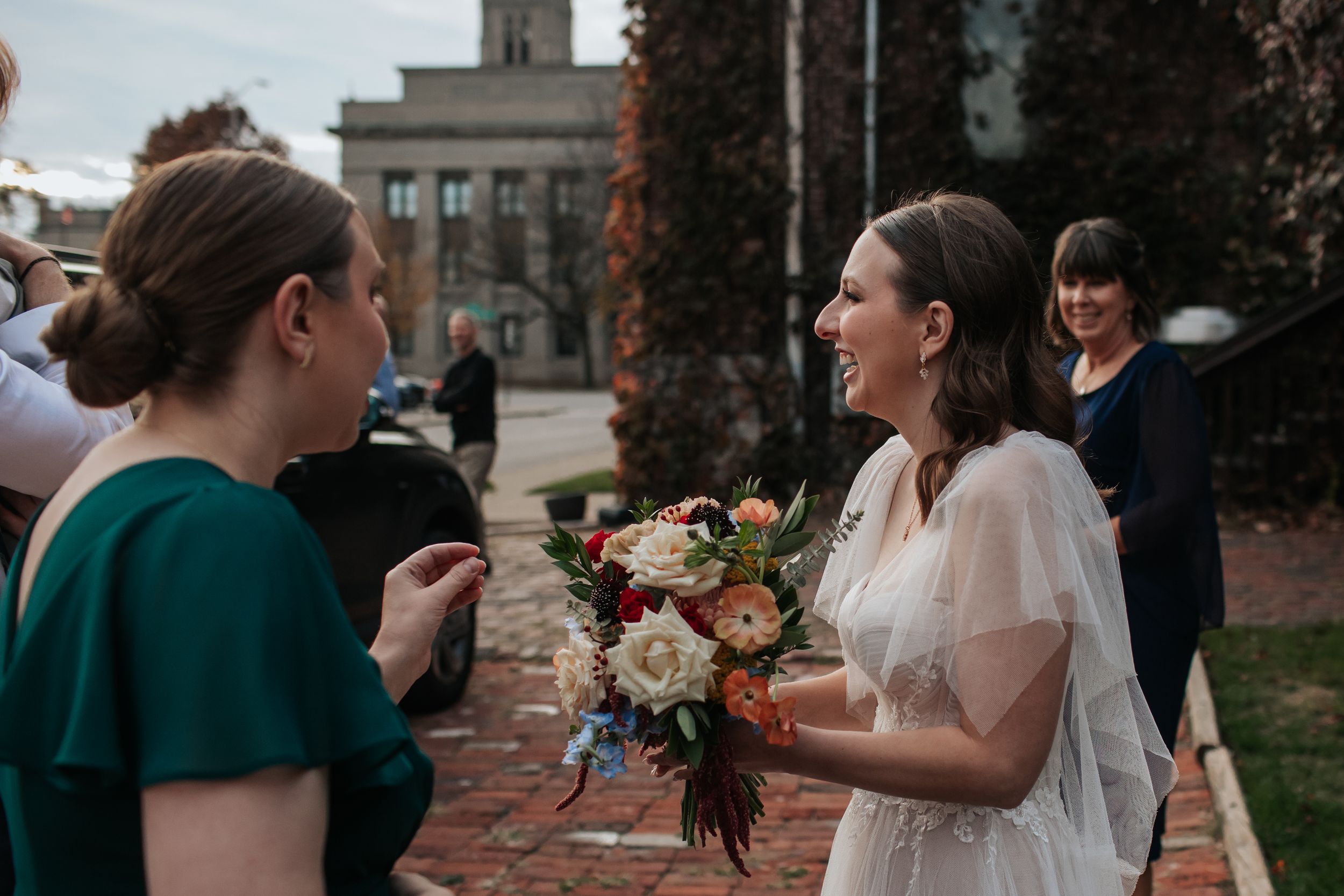 A wedding party stands together outdoors during a fall ceremony with autumn foliage in the background.