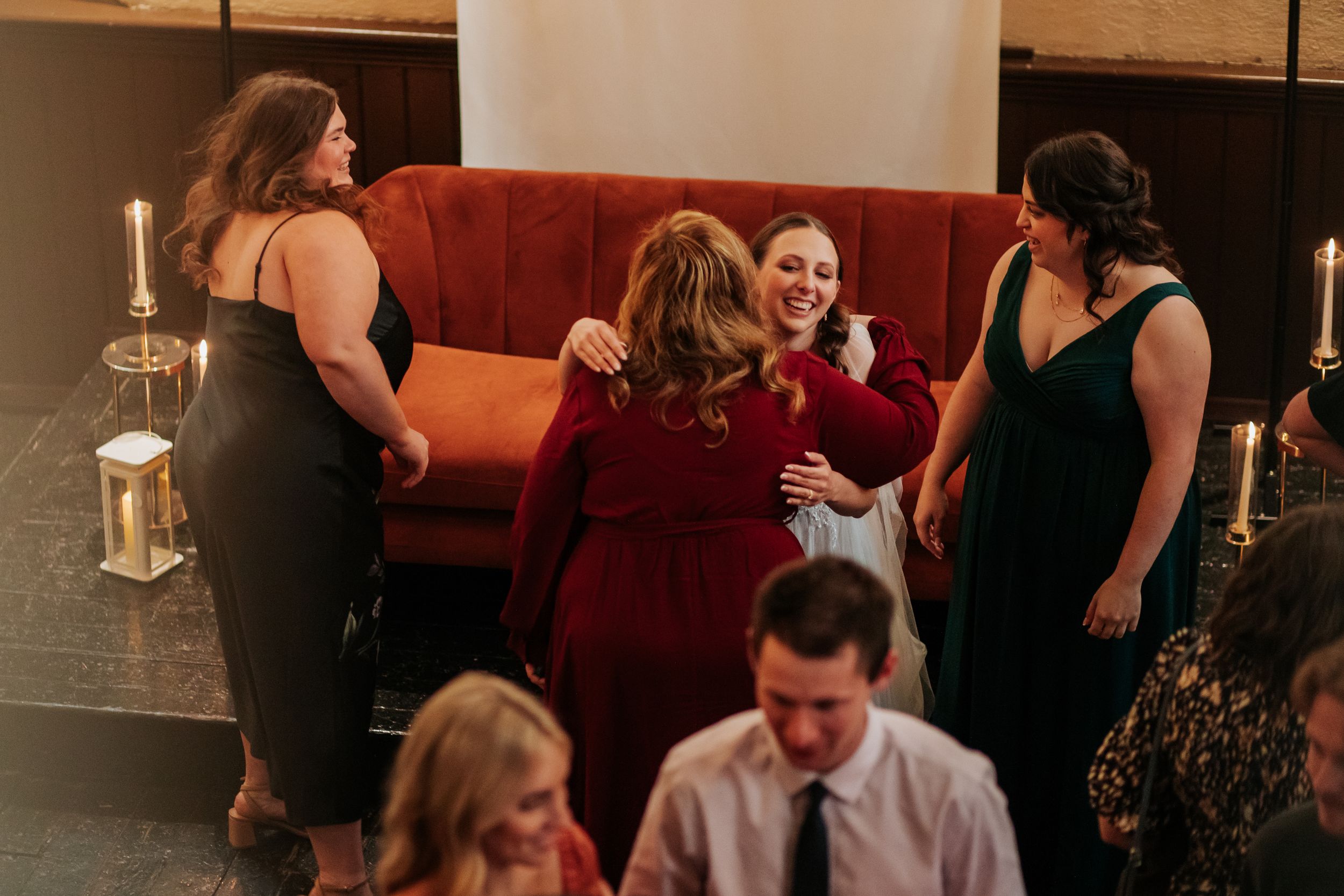 A candid moment at a lively wedding reception with guests mingling and dancing in a dimly lit venue.