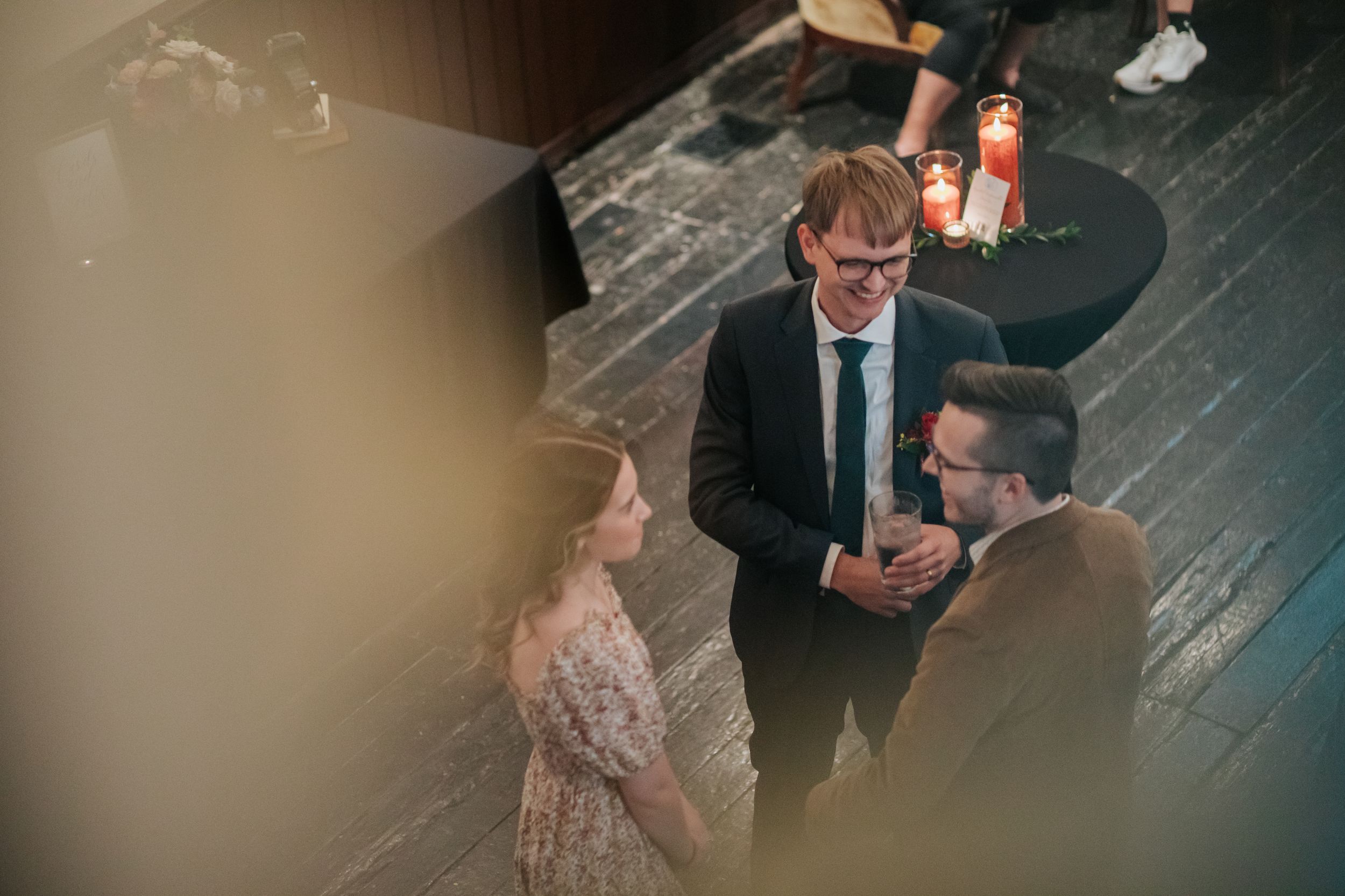 Three people engaged in conversation at a social gathering on a dark wooden floor.