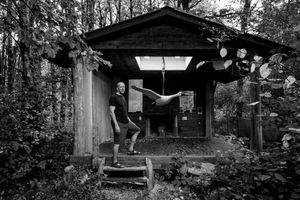 A series of abandoned wooden cabins and structures in a wooded area create an eerie atmosphere in black and white.