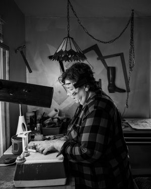 A person in a plaid shirt works at a desk in moody black and white lighting.