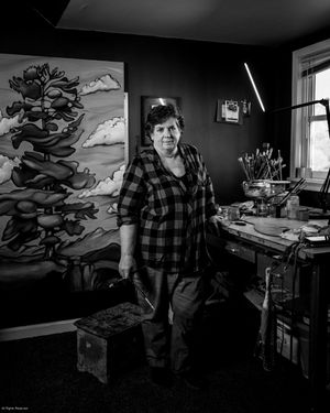 Artist works in dark studio with dramatic black and white mural artwork covering walls in moody lighting.