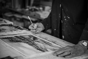 A person's hand writing or drawing on paper with a pen in black and white.