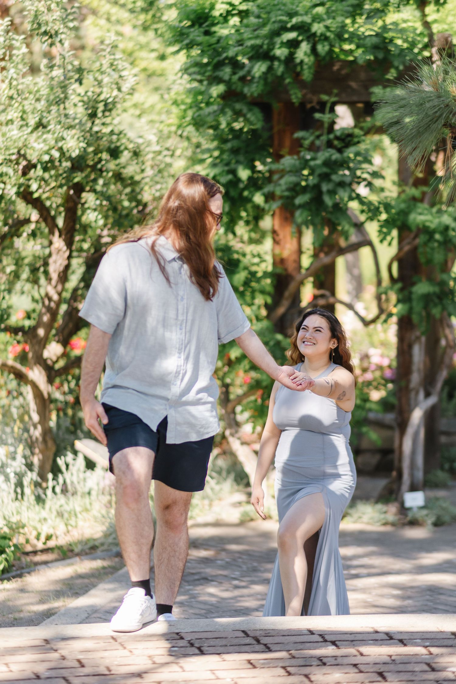 Engagement photoshoot for a couple on a stone path surrounded by lush green trees at the Ornamental Gardens in Summerland, BC