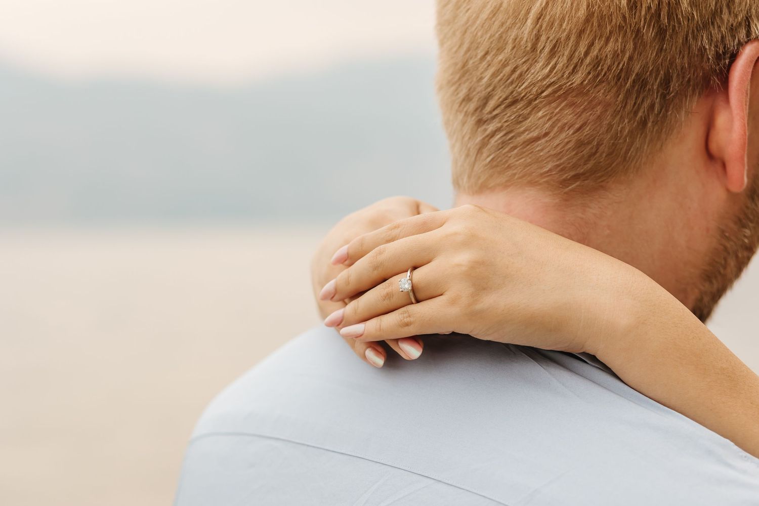 Couple posing for engagement photos with a close up of the engagement ring in West Kelowna BC with a view of Okanagan Lake in the background