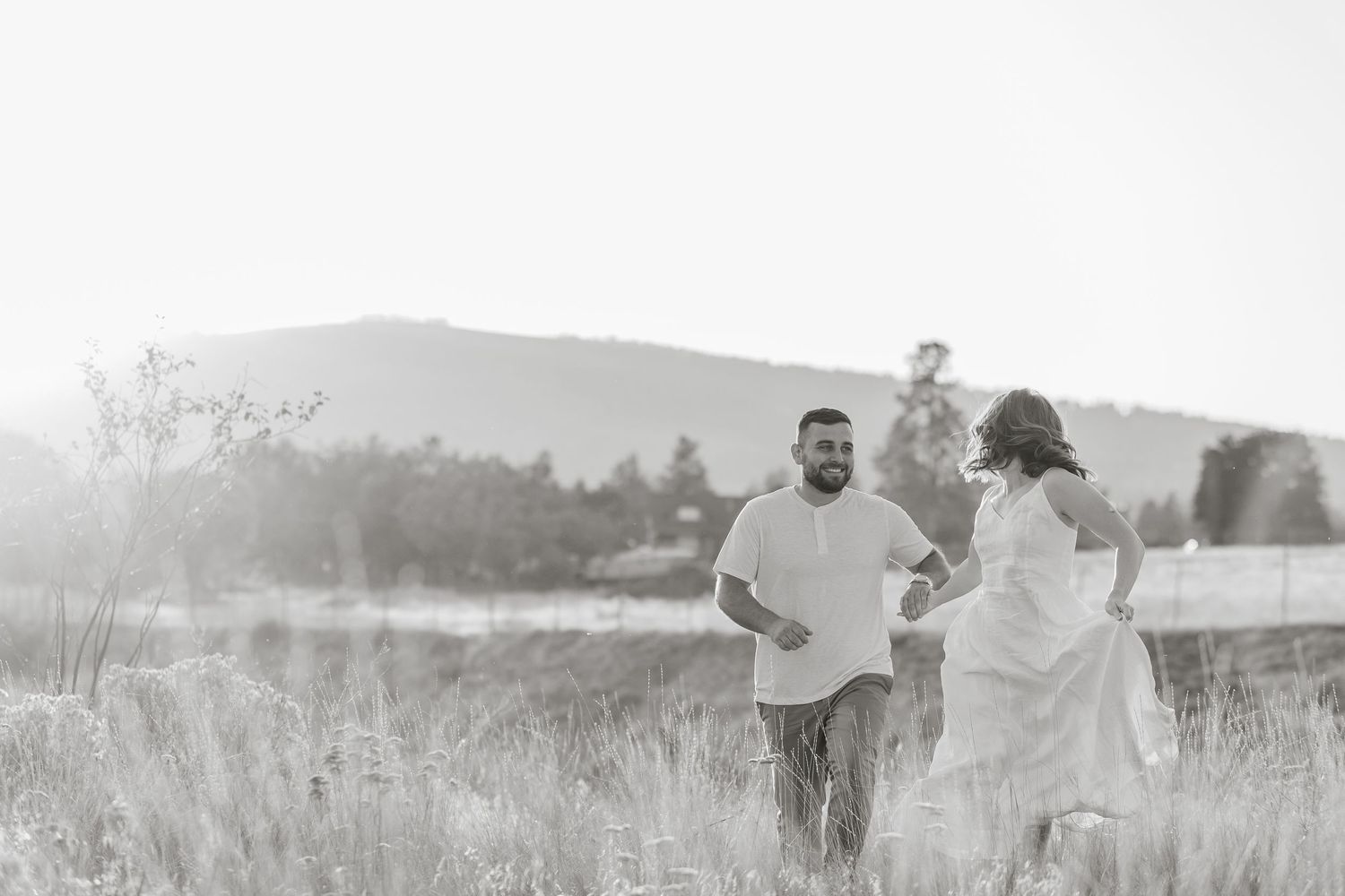 Black and White photo's of a couple walks hand in hand through a misty meadow during a romantic golden hour photoshoot in West Kelowna, BC.
