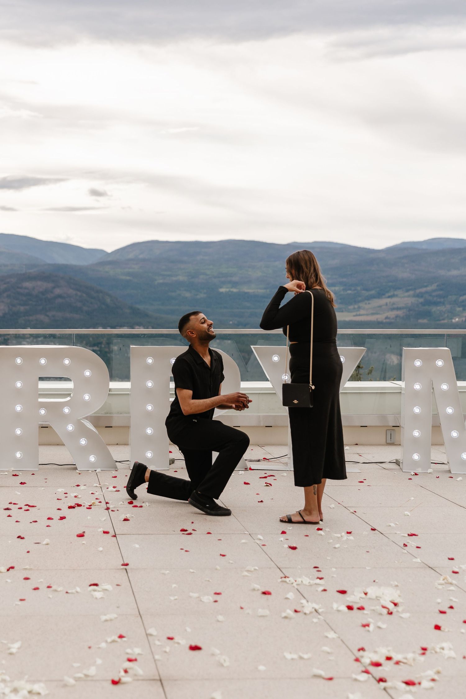 A romantic proposal scene on a rooftop deck overlooking mountains in the Okanagan at sparking hills resort for a photoshoot