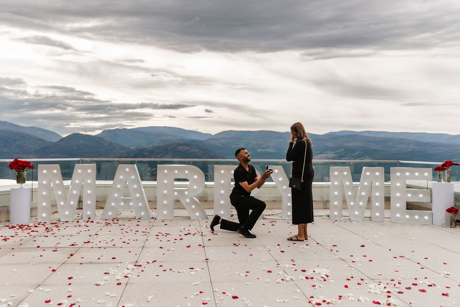 A couple sharing a special moment on a scenic rooftop with mountains in the background and rose petals at Sparkling hills for a proposal