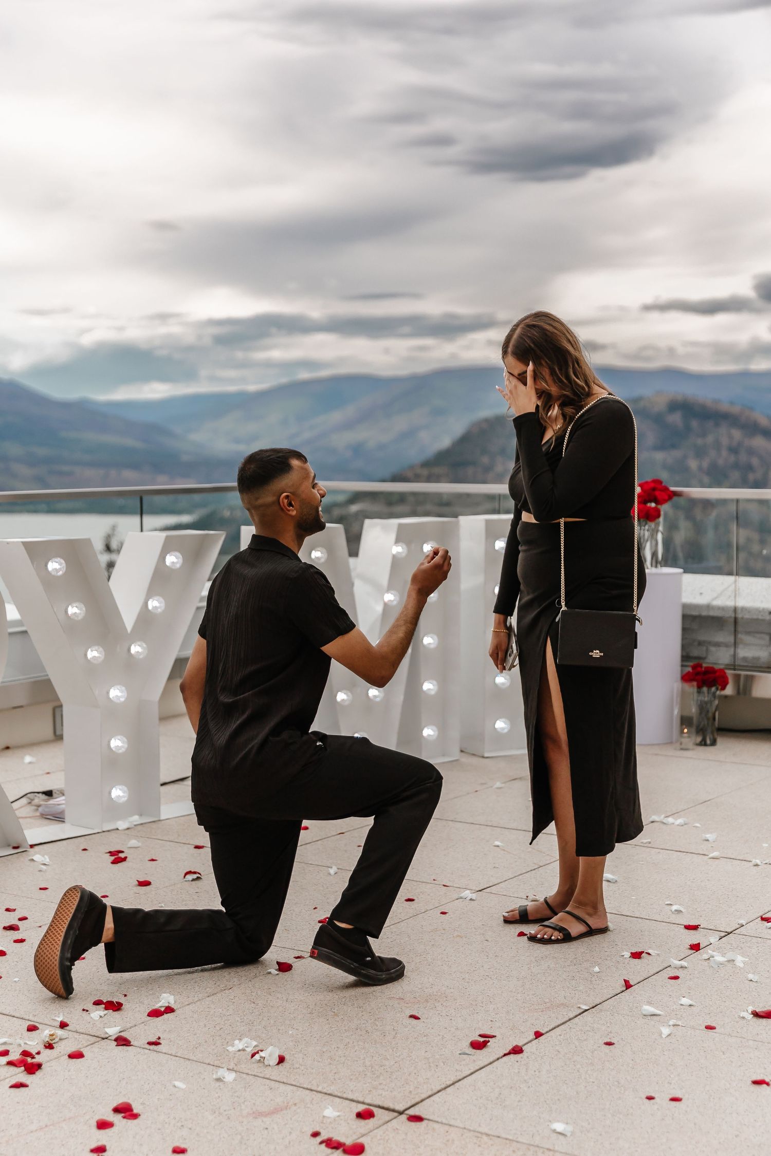 A romantic proposal moment on a mountain viewpoint with lit letters and rose petals scattered on the ground in Kelowna bc at sparkling hills