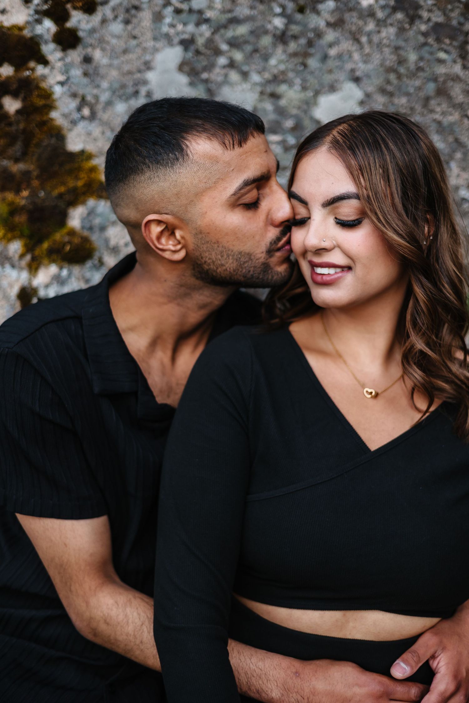 A tender moment between a couple dressed in black against a rustic stone backdrop at sparkling hills for a surprise proposal photoshoot