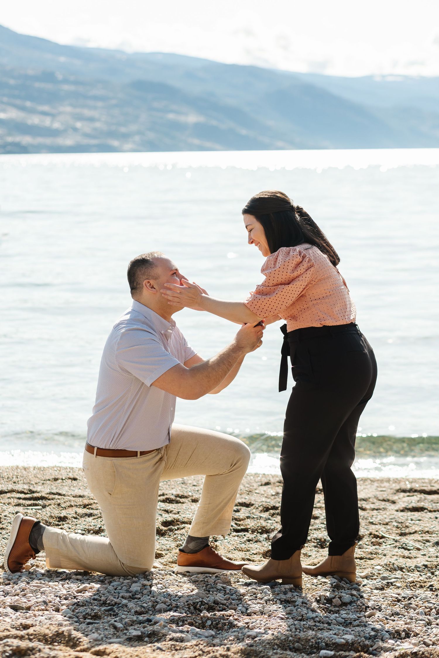 Surprise proposal photo of a couple during an engagement session with Okanagan lake and mountains in the background.