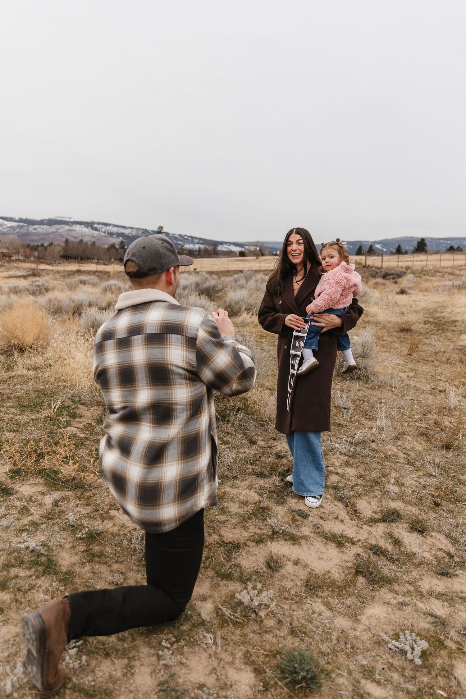 A couple shares a moment in a field with brown grass hills in the background during surprise proposal photoshoot in West Kelowna, BC.