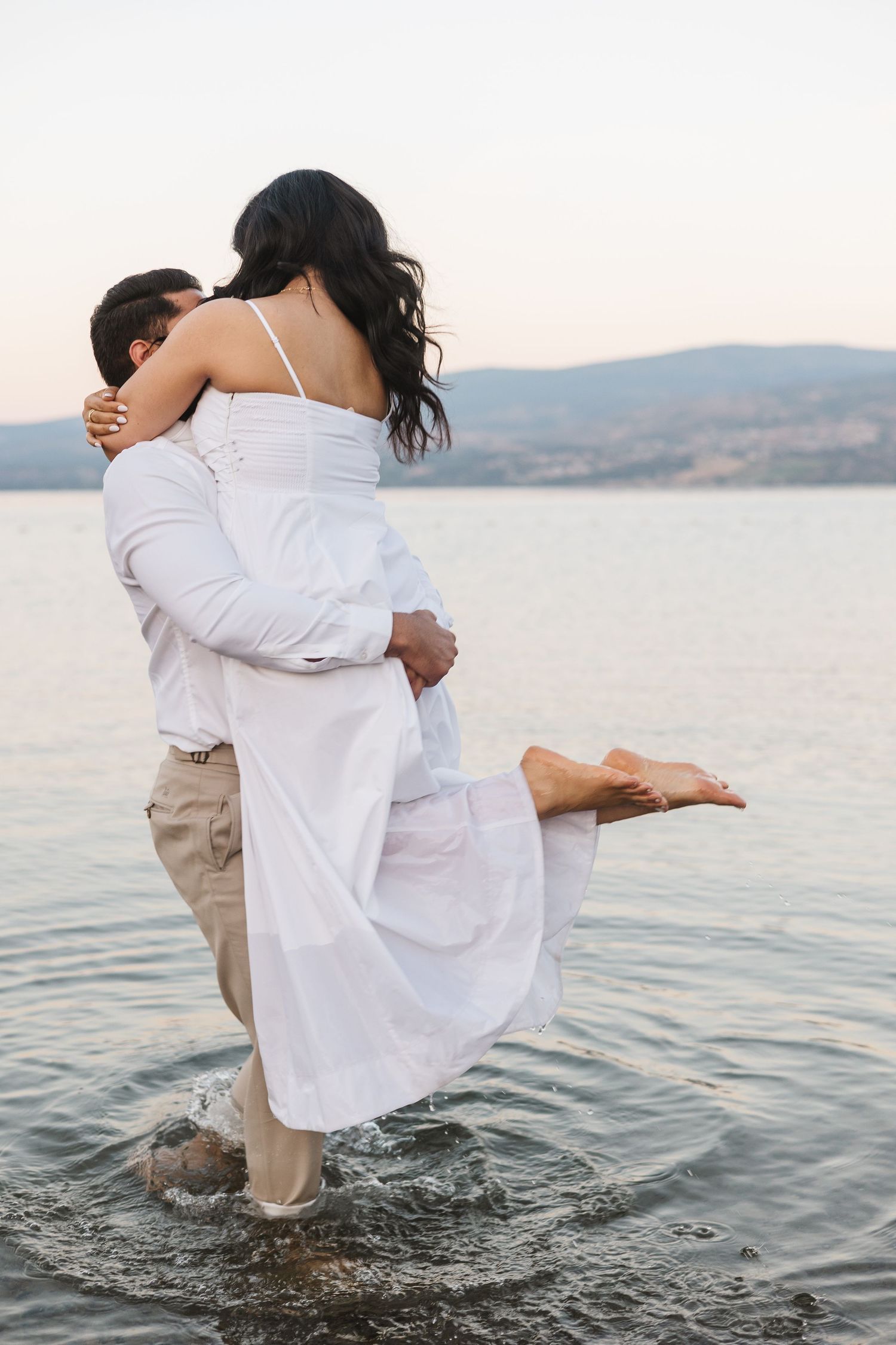 Couple photos splashing in the lake in Kelowna, BC for an engagement session at sunset with a view of the lake and mountains.