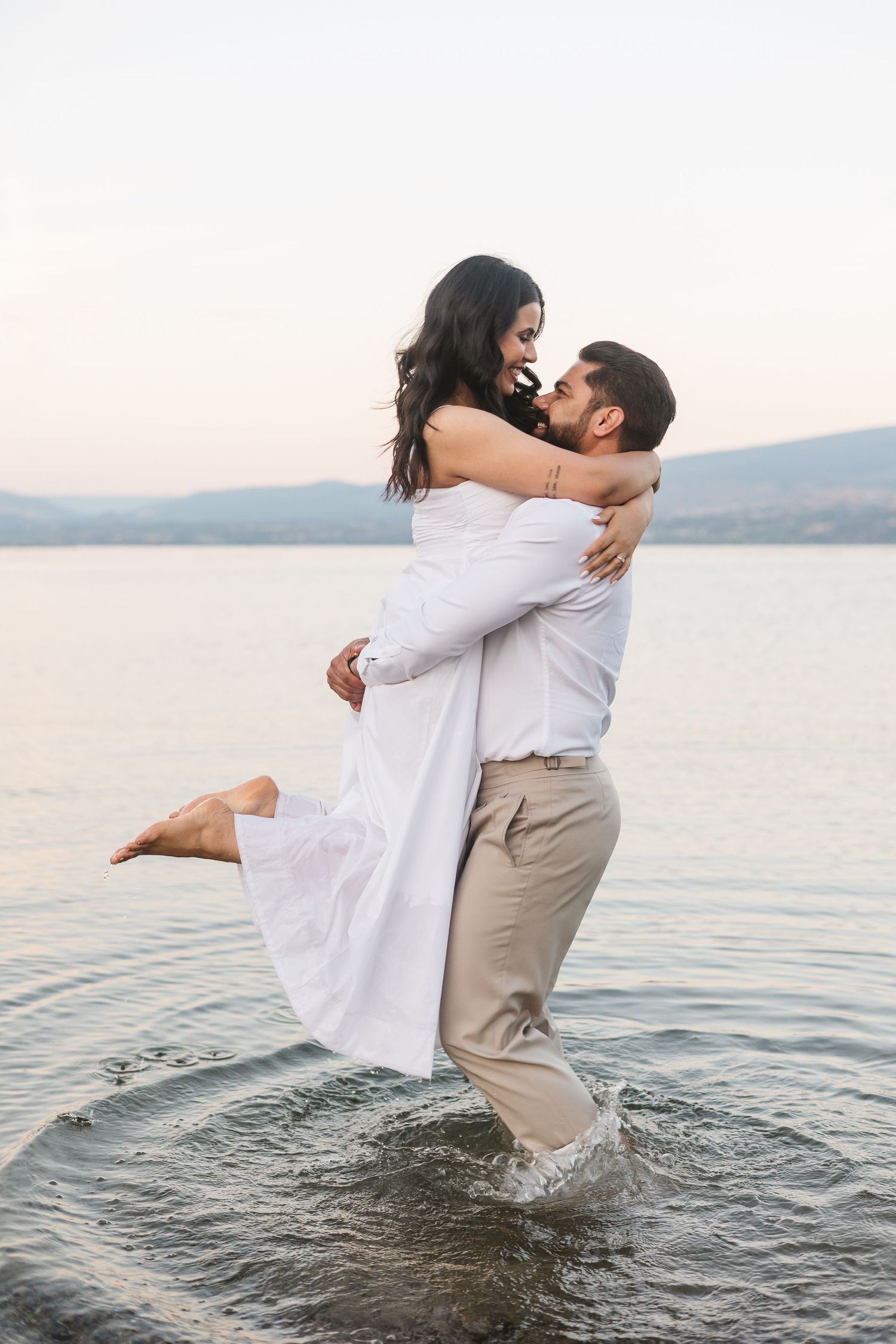 Couple photos in the lake in Kelowna, BC for an engagement session at sunset with a view of the lake and mountains.