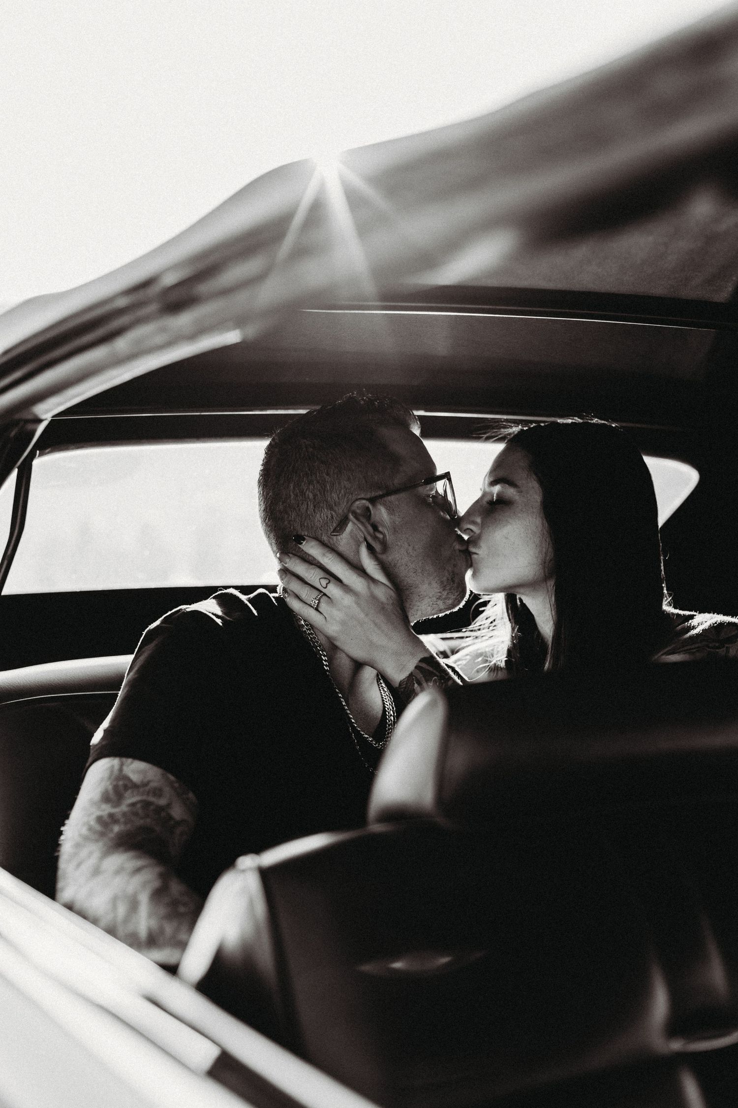 Black and white photo of two people sitting in a car interior with dramatic lighting and shadows in kelowna for a couples photoshoot