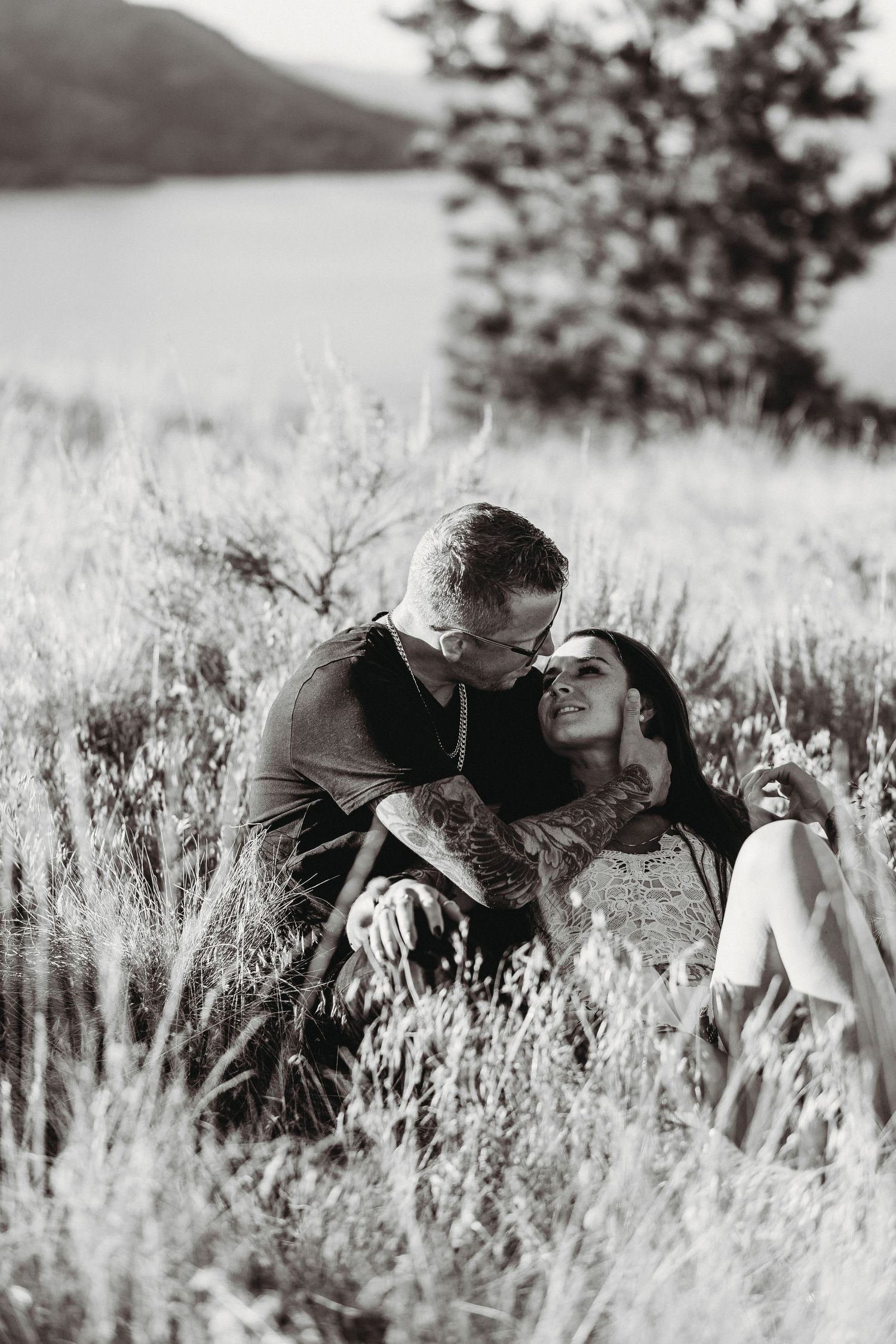 Couple laying together in a sunlit meadow surrounded by tall grass and wildflowers at Knox mountain for an engagement session