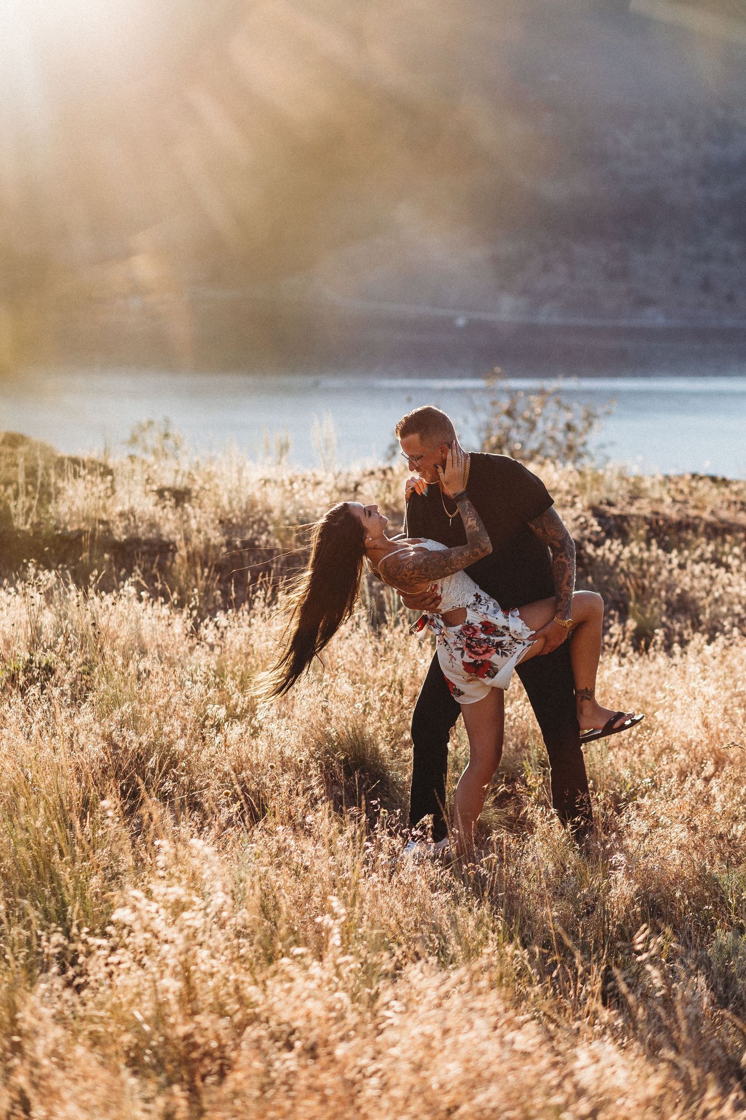 Couple playfully interacting in a golden field at sunset with tall grass swaying in the warm light for an engagement session in Kelowna
