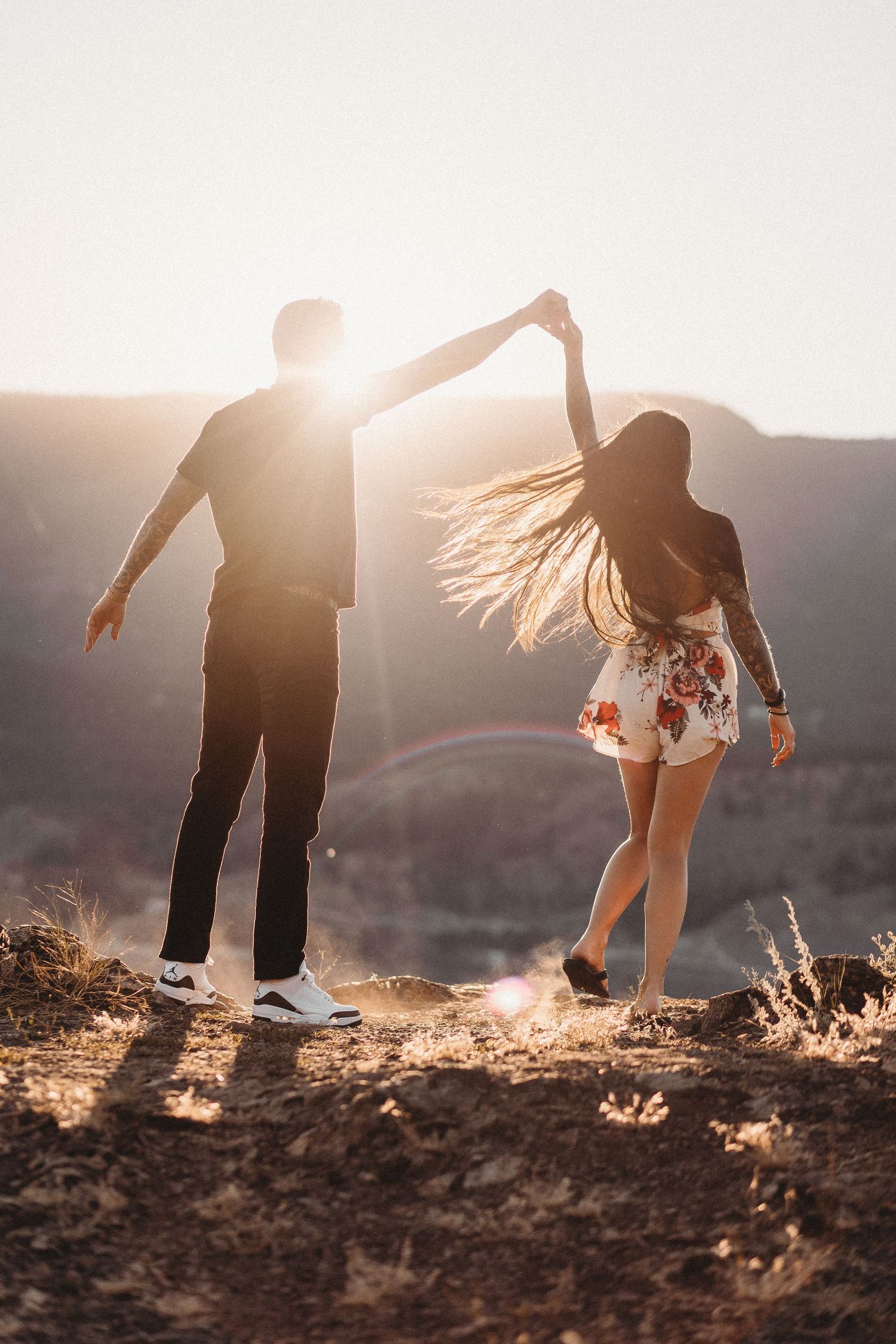 Silhouetted couple dancing together on a hilltop during golden hour with flowing hair and dramatic backlighting at Knox mountain in Kelowna