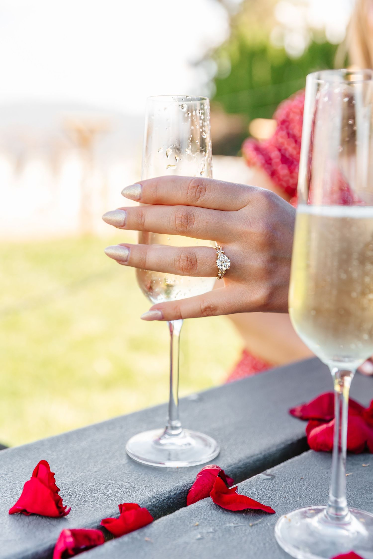 A hand wearing an engagement ring holds a champagne after surprise proposal photos in West Kelowna at a winery