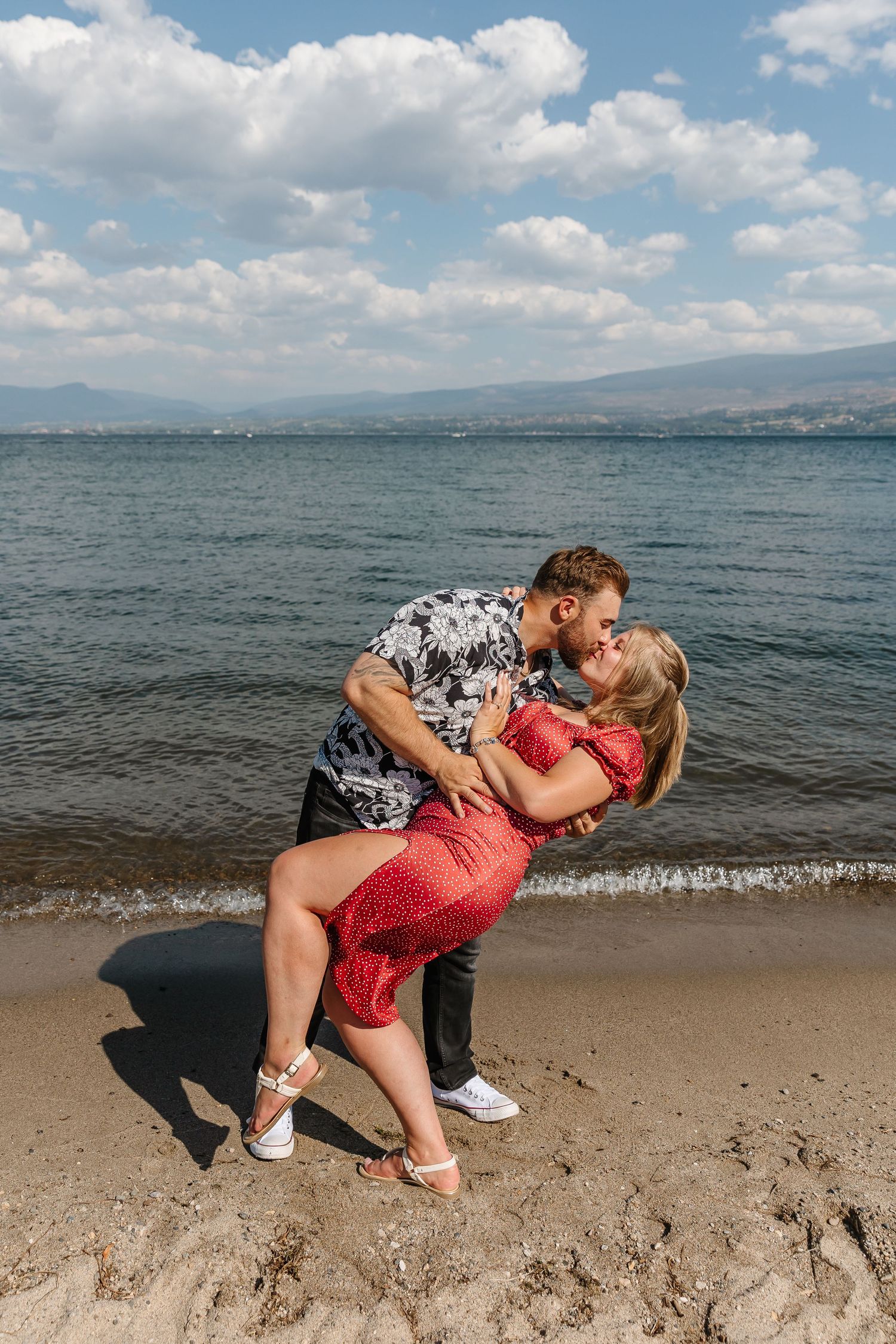 A couple kissing after surprise proposal engagement photos with okanagan lake in the background and view of the mountains