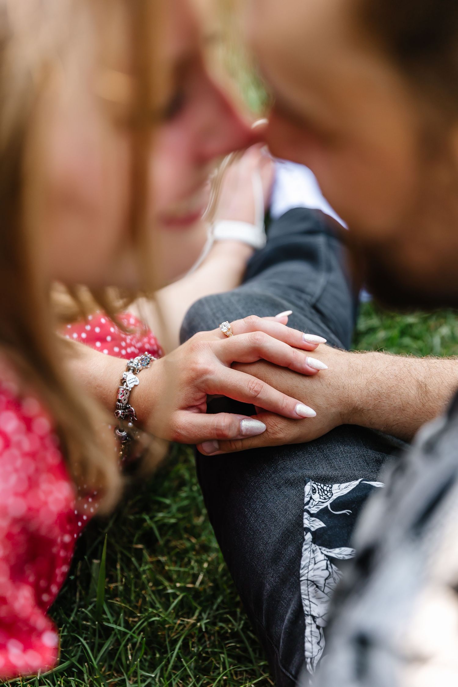 Close up of hands touching on grass with a diamond ring visible, showing a romantic engagement moment at frind winery in West Kelowna