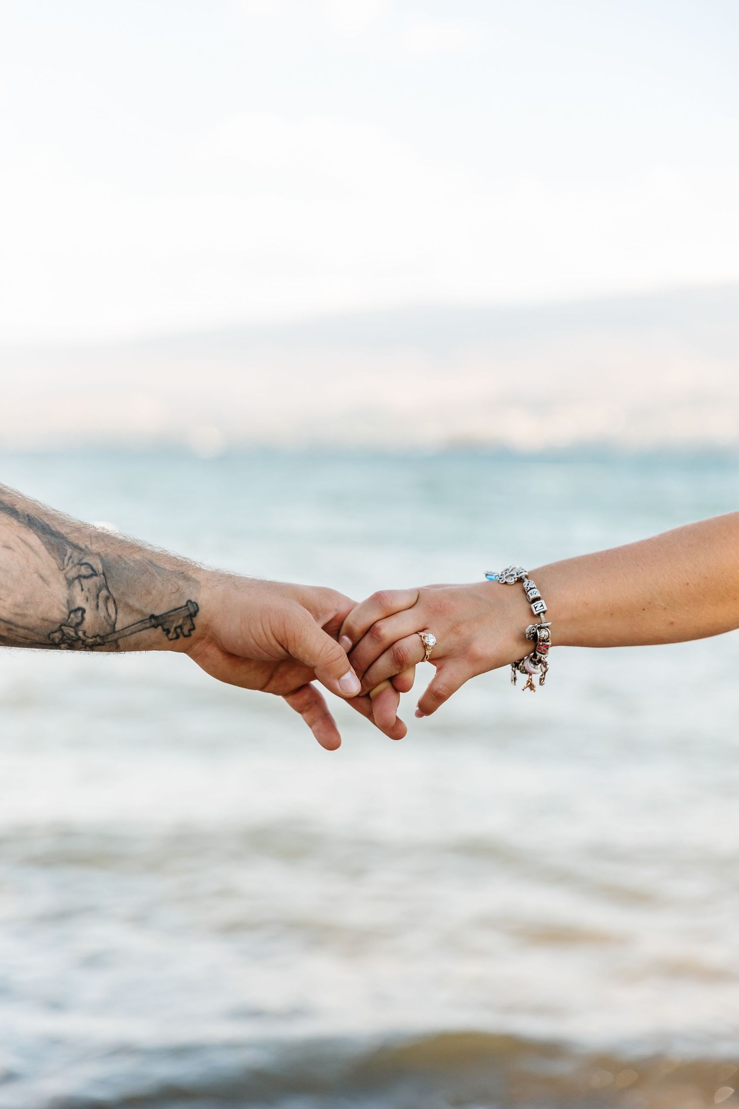 Two hands reaching towards each other with rings and bracelets against okanagan lake for a surprise proposal photoshoot