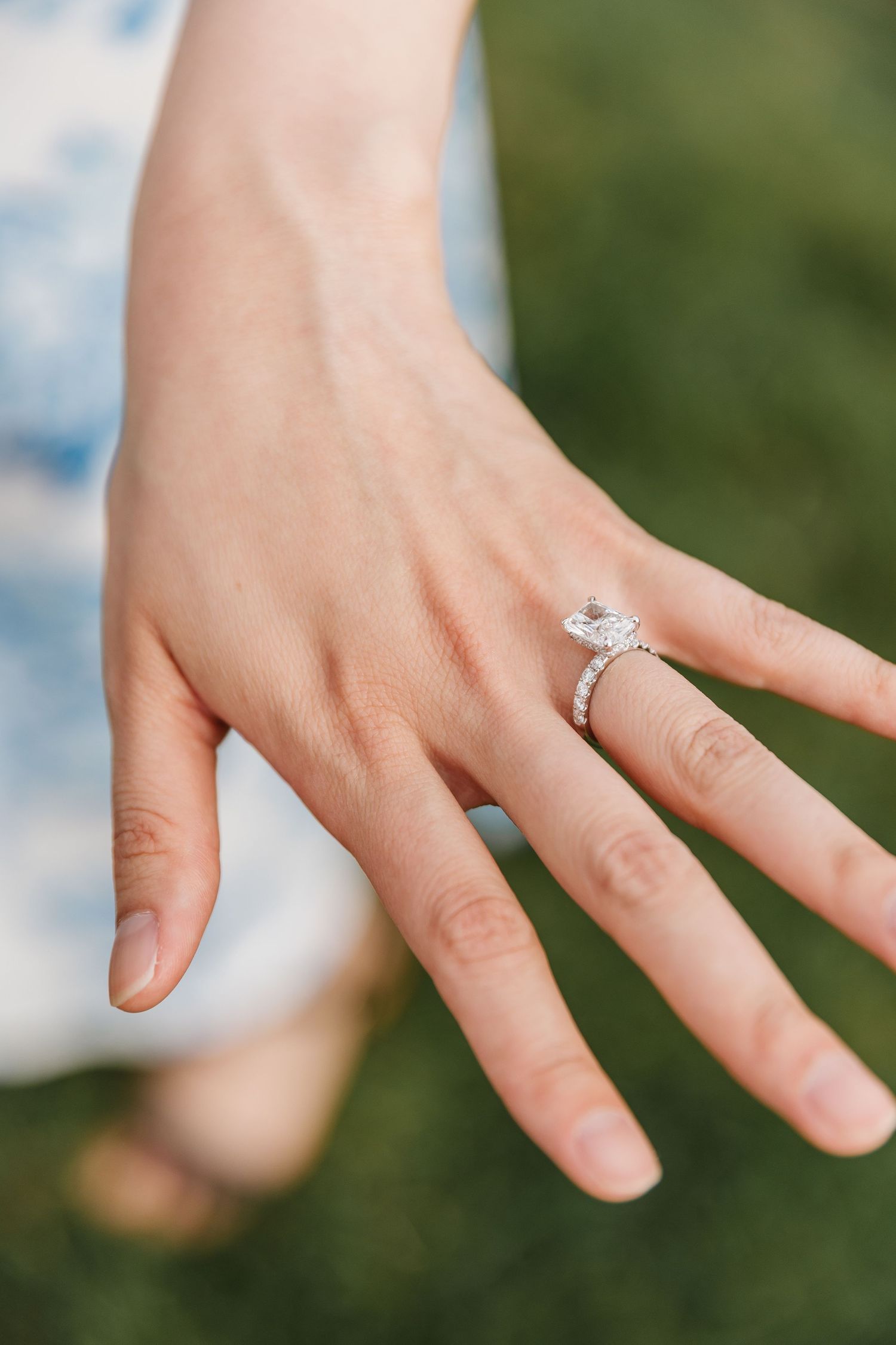 Close-up view of a sparkling diamond engagement ring on a woman's hand against a blurred green background in West Kelowna, BC for photoshoot
