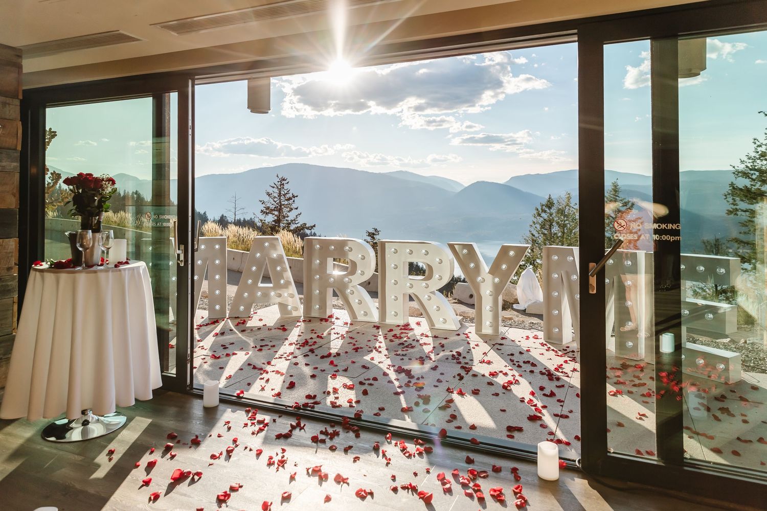 Large MARRY ME text display with rose petals scattered on floor by mountain view windows at scenic venue Sparkling Hills Resort in Kelowna