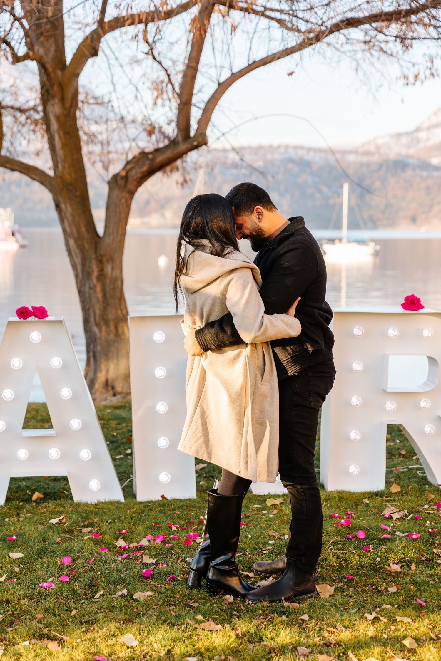 A romantic surprise proposal photography session under trees with large white marquee signs letters spelling out MARRY ME in Kelowna BC