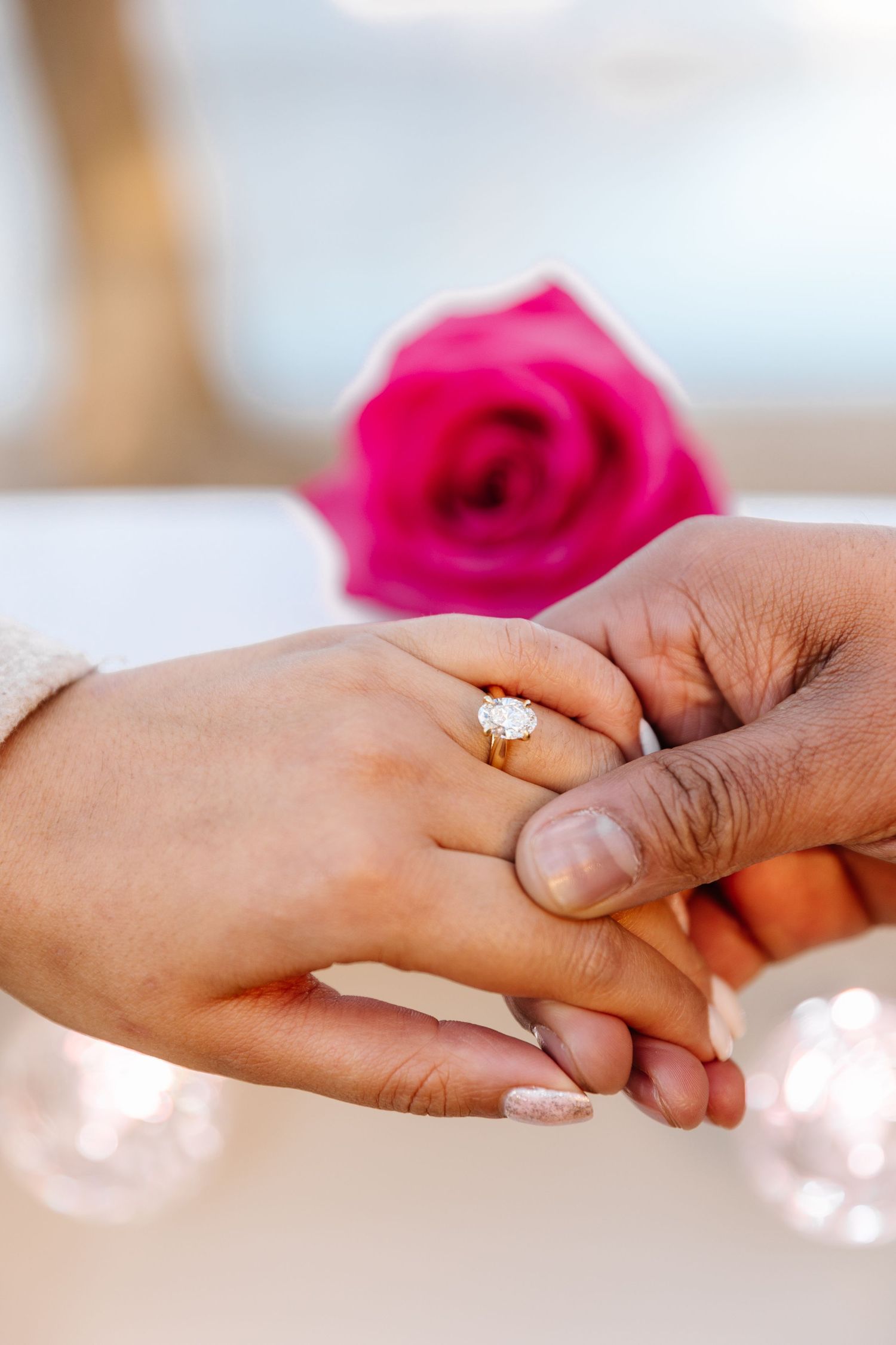 Close-up sequence of hands holding each other with engagement ring and pink roses in soft focus background in Kelowna BC for a photoshoot
