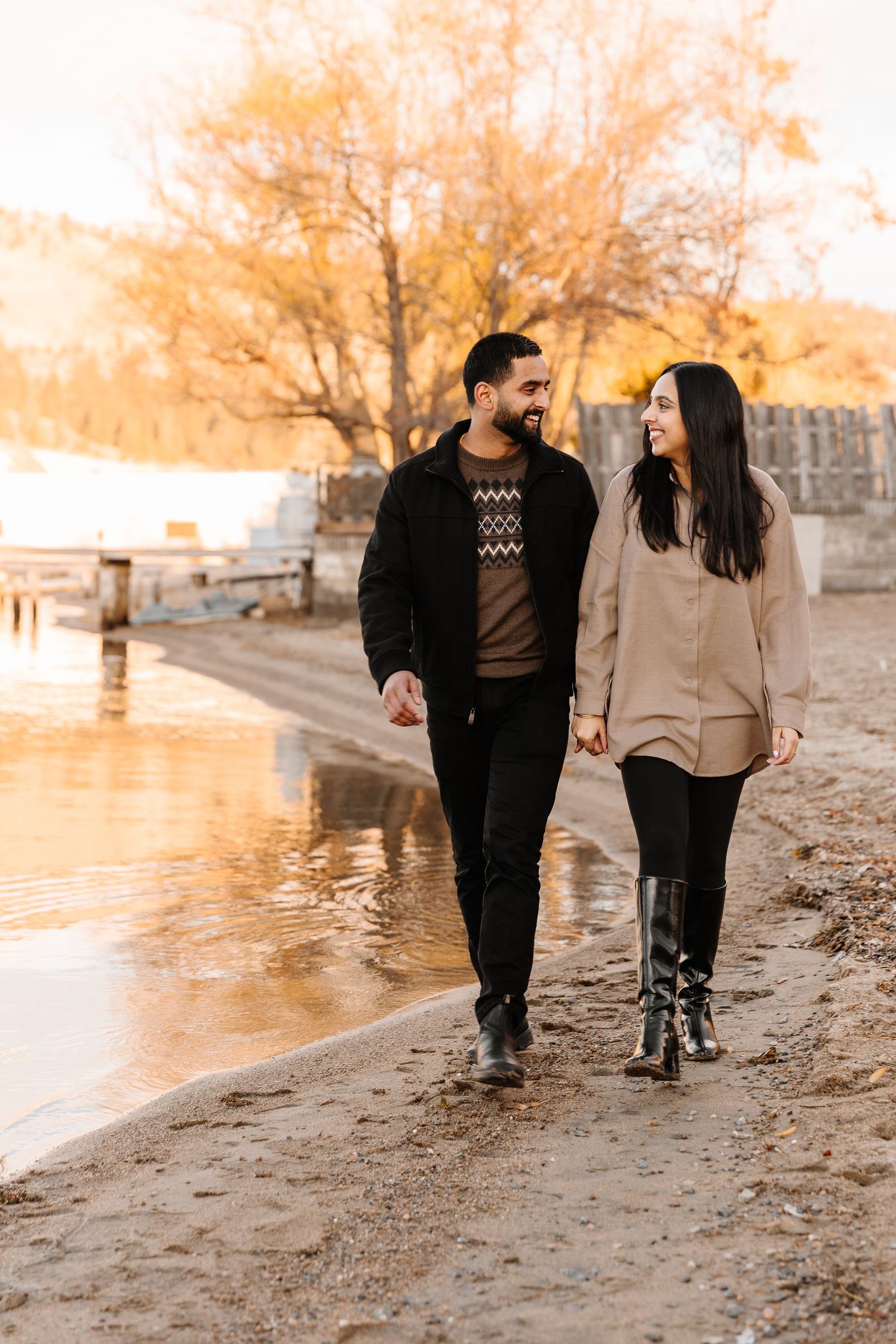 A couple takes a romantic stroll along a riverbank path during golden hour on an autumn afternoon in Kelowna BC for an engagement photoshoot