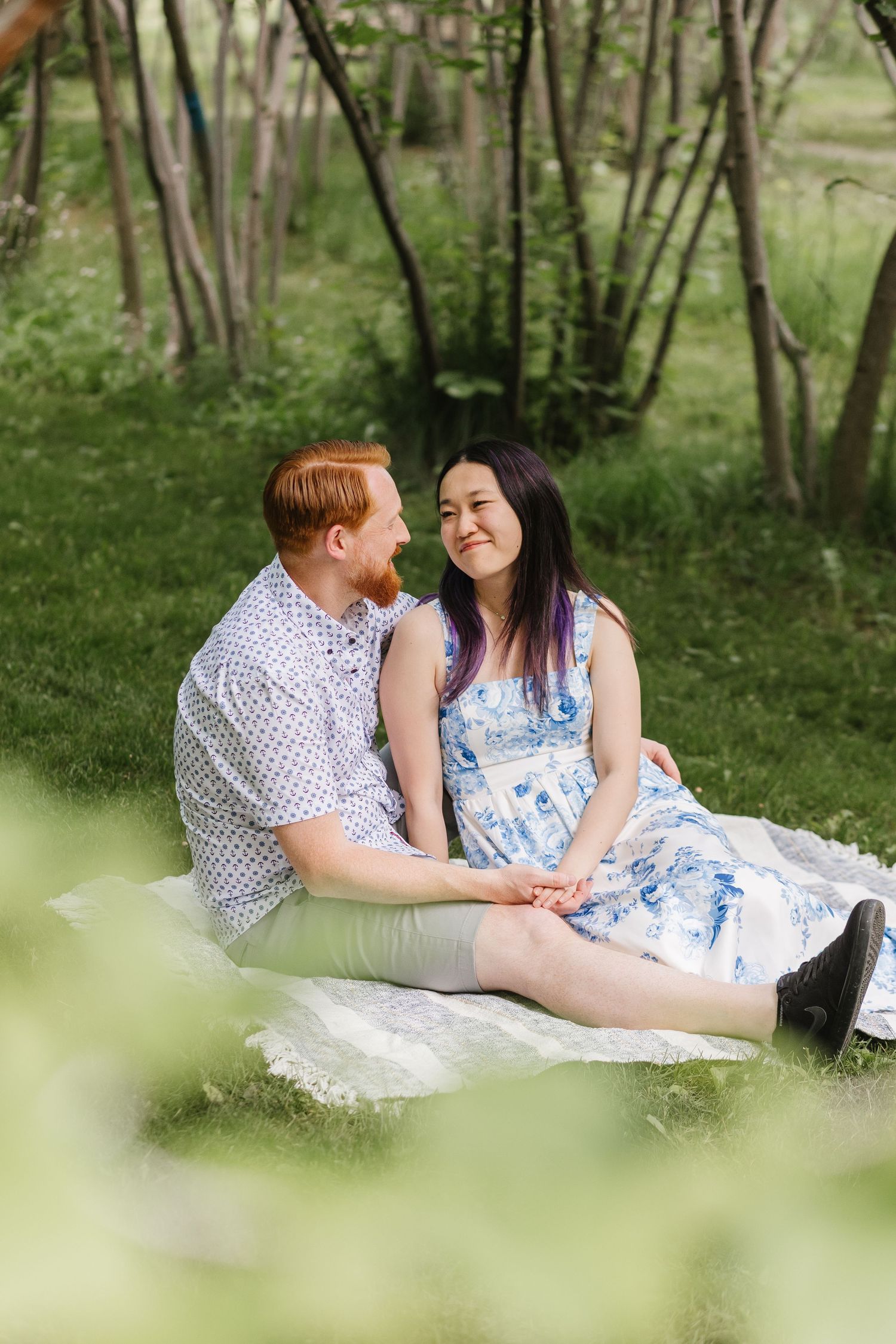 A couple relaxes on a white blanket in a tranquil wooded setting during an engagement photoshoot at Gellatly Nut Farm in West Kelowna, BC.