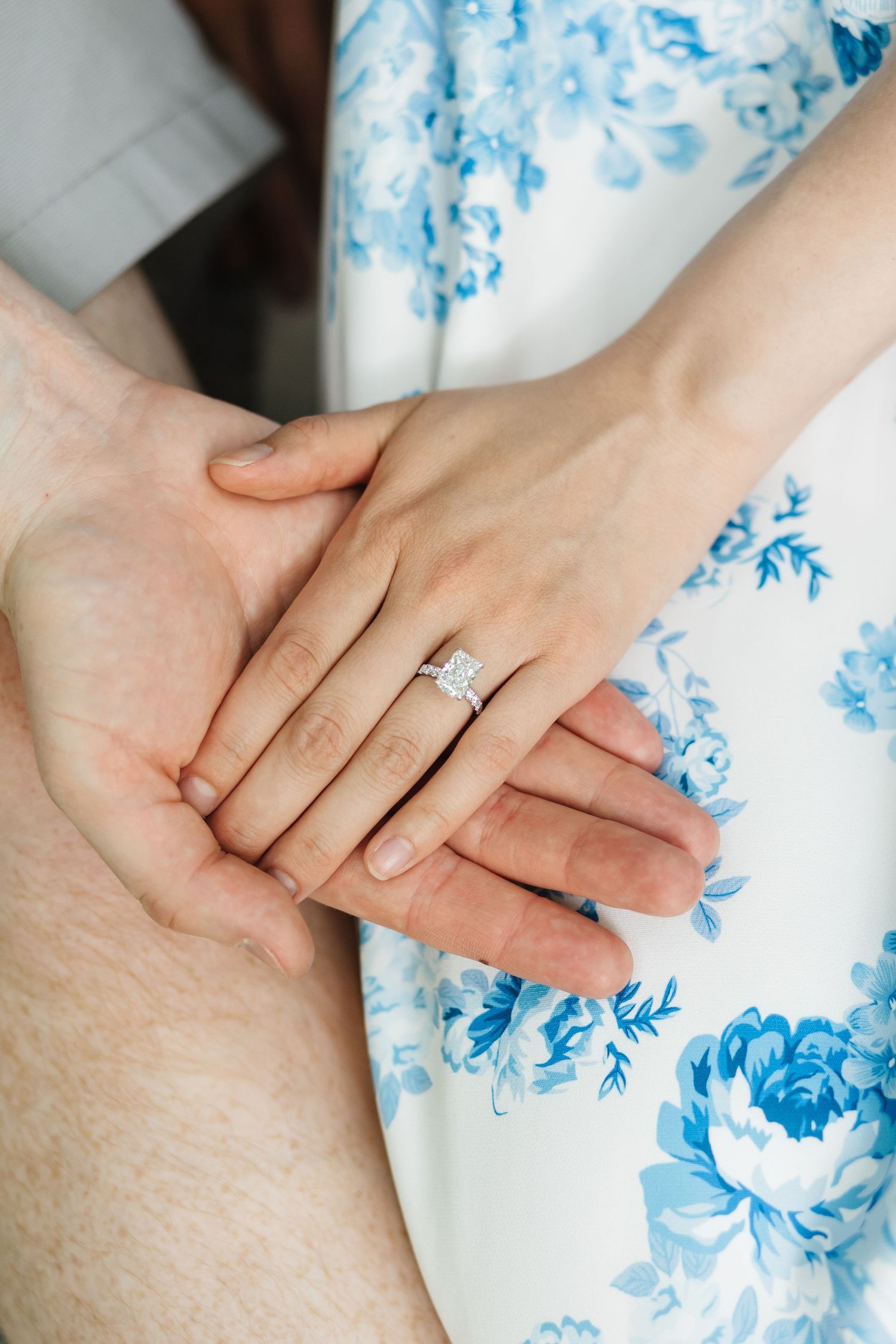 Detail shots of hands displaying an engagement ring against a white and blue floral dress background in West Kelowna, BC