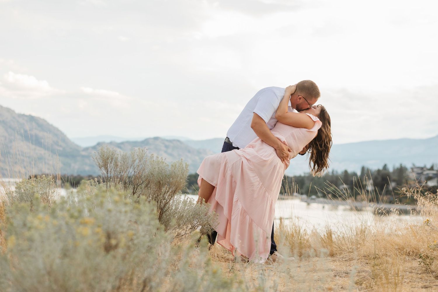 Engagement photos taken in a golden field at sunset with mountains in background at Sanctuary Gardens in West Kelowna, BC