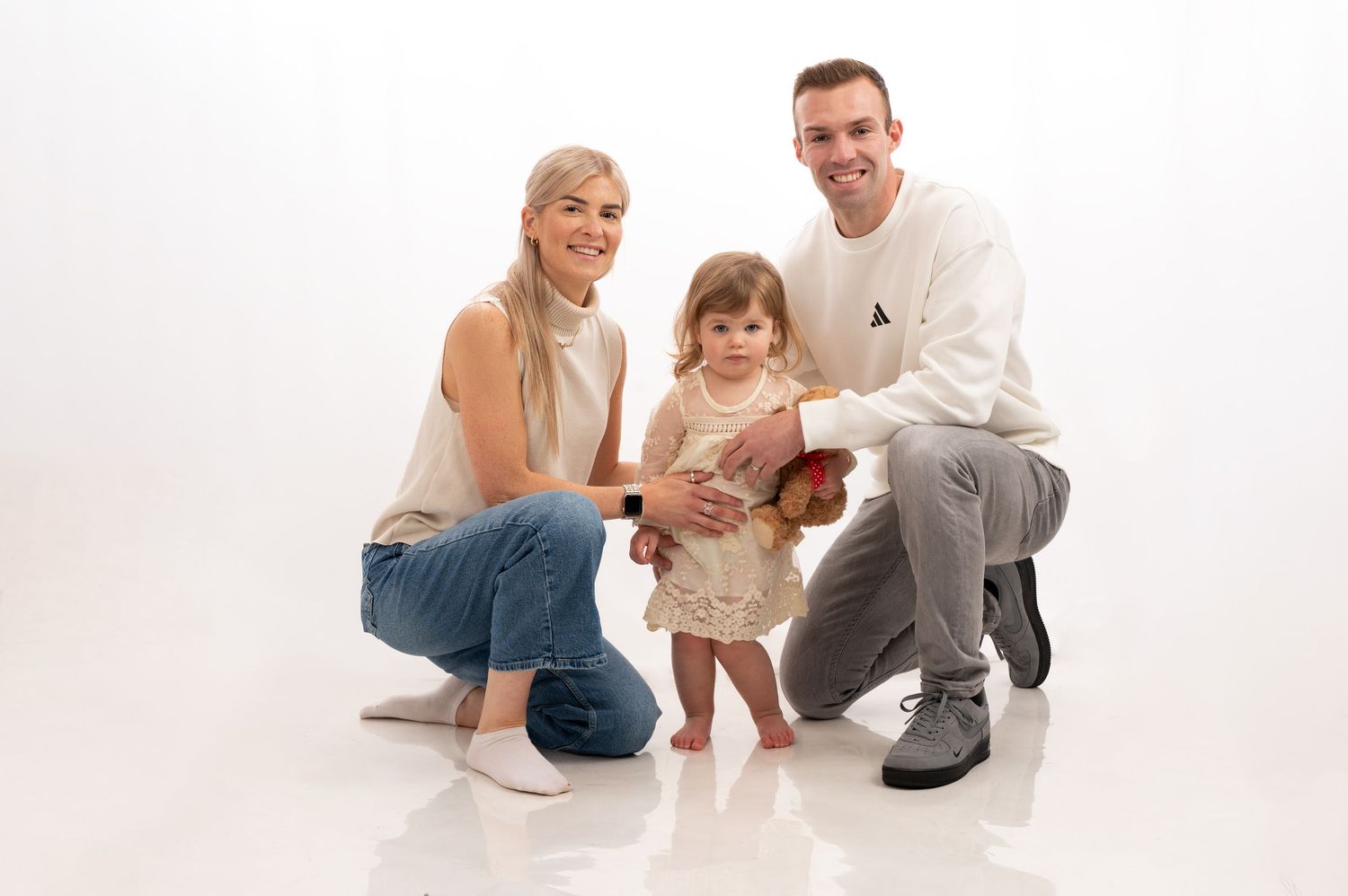 A family poses together in casual white outfits against a light background in a series of connected photos.