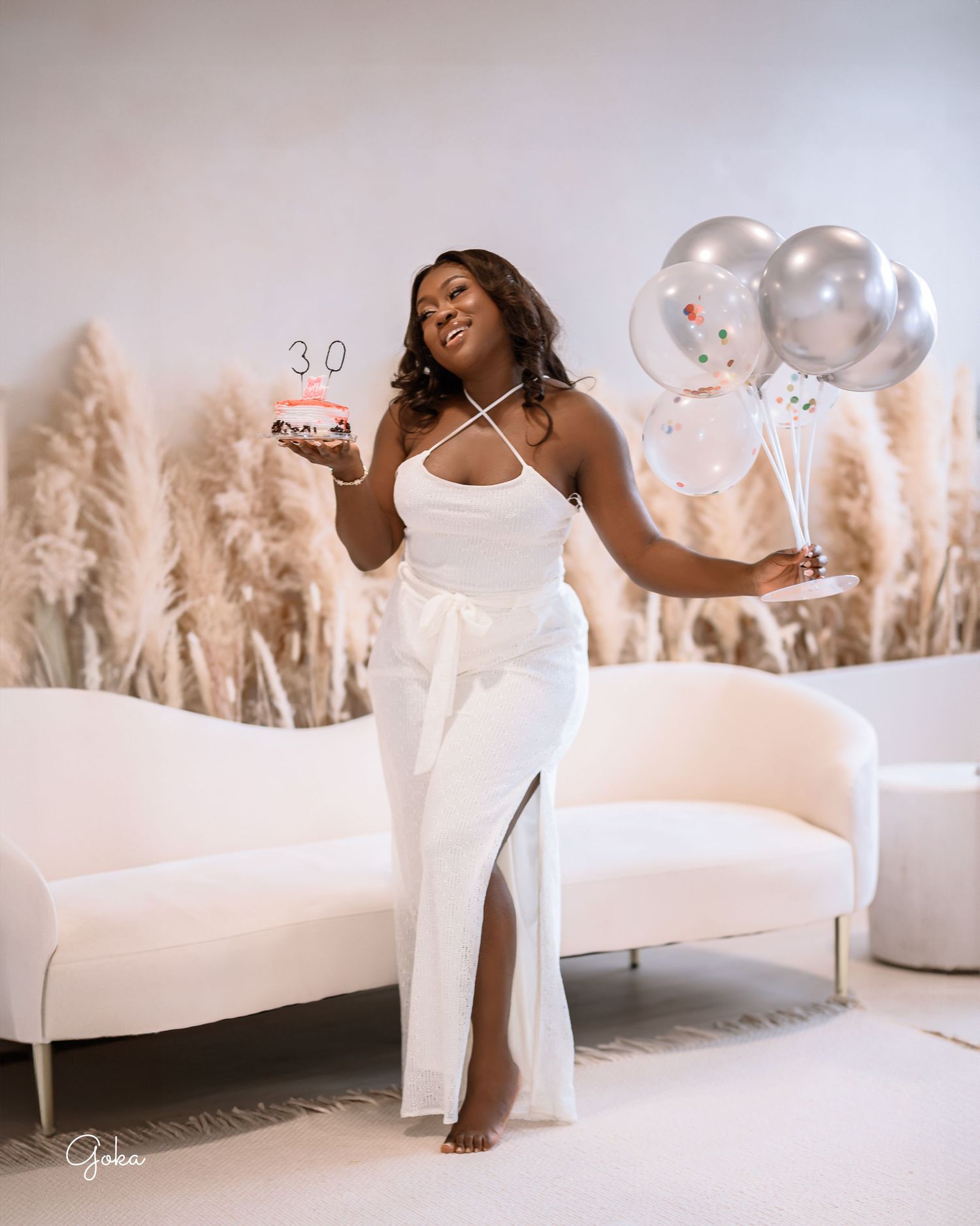 A figure in a flowing white dress poses gracefully against a backdrop of pampas grass in a dreamy outdoor setting.