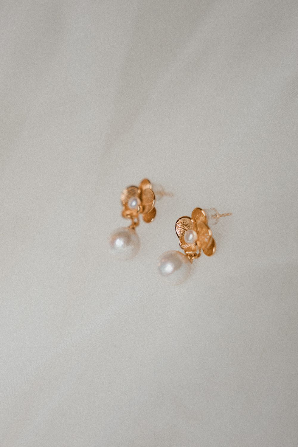 Delicate pearl stud earrings with gold-toned settings photographed from different angles on a light gray background.