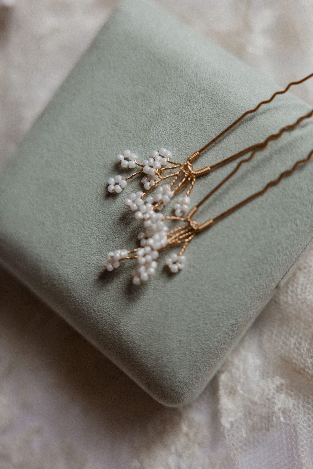 Delicate pearl and crystal hair pins resting on a soft sage green velvet cushion display elegant bridal accessories.