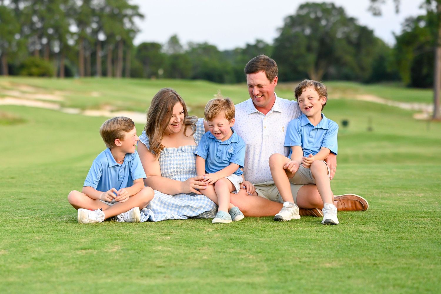 Family sitting together on a lush green golf course on a sunny summer day.