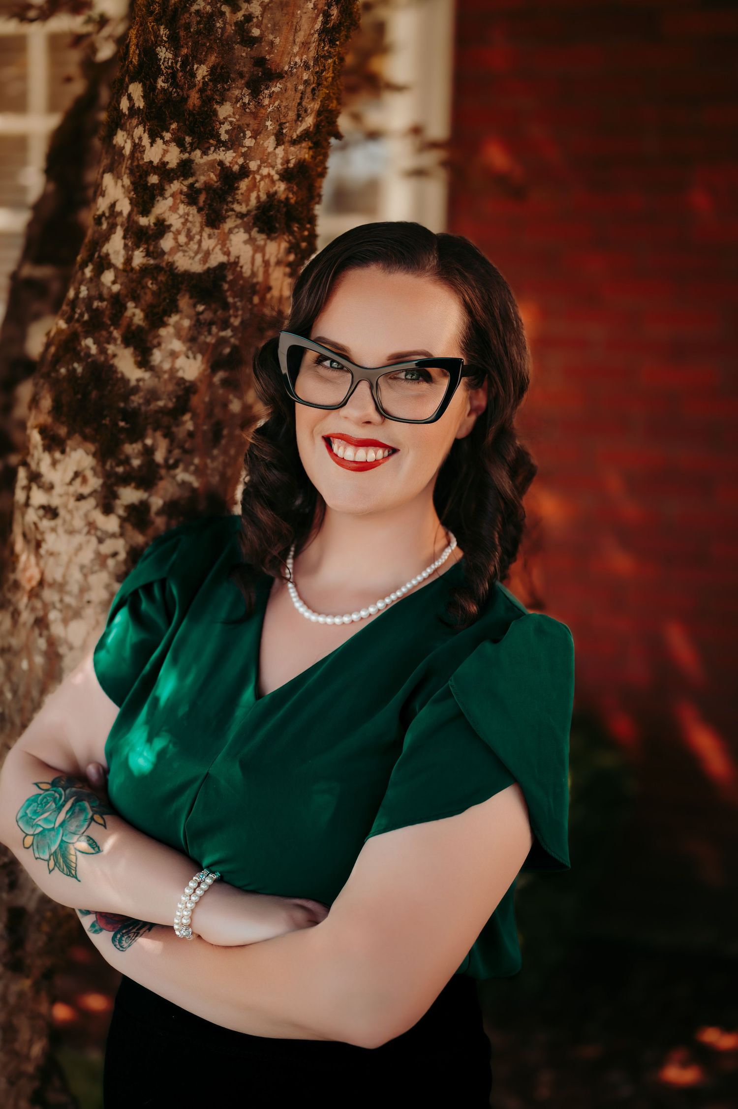 Portrait of person in emerald green dress with glasses against dramatic red background.