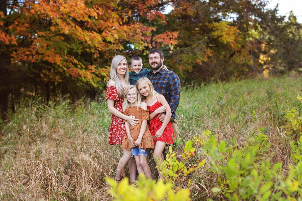 A family enjoying a playful autumn photoshoot together in a field with vibrant fall foliage.
