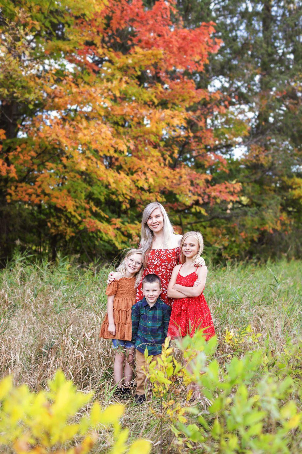Beautiful fall foliage with vibrant red and yellow maple leaves frames a family portrait session in a grassy meadow.