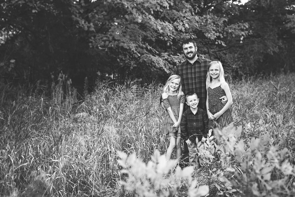 Black and white photo of a family posing together outdoors in a natural setting with tall grass.
