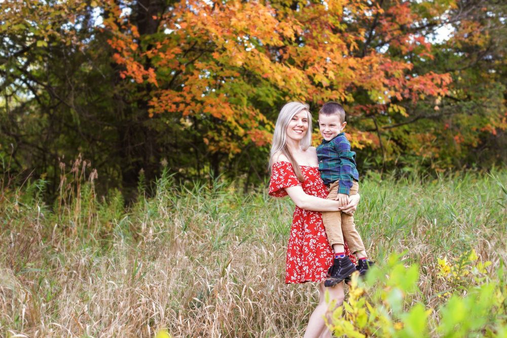 A scenic autumn outdoor portrait in a field with tall grass and vibrant orange fall foliage in the background.