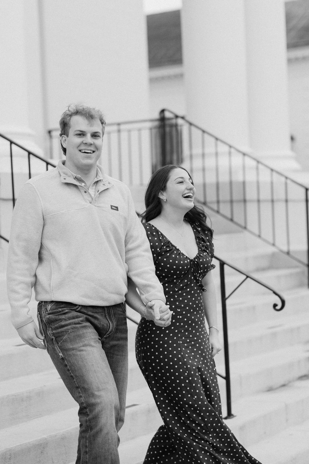 A couple shares a candid laughing moment together in black and white on outdoor steps.