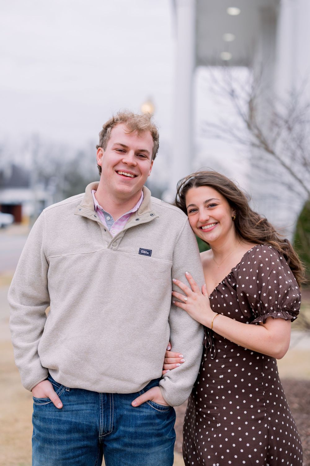 A couple in casual attire embraces and smiles outdoors during a photo session in cool weather.